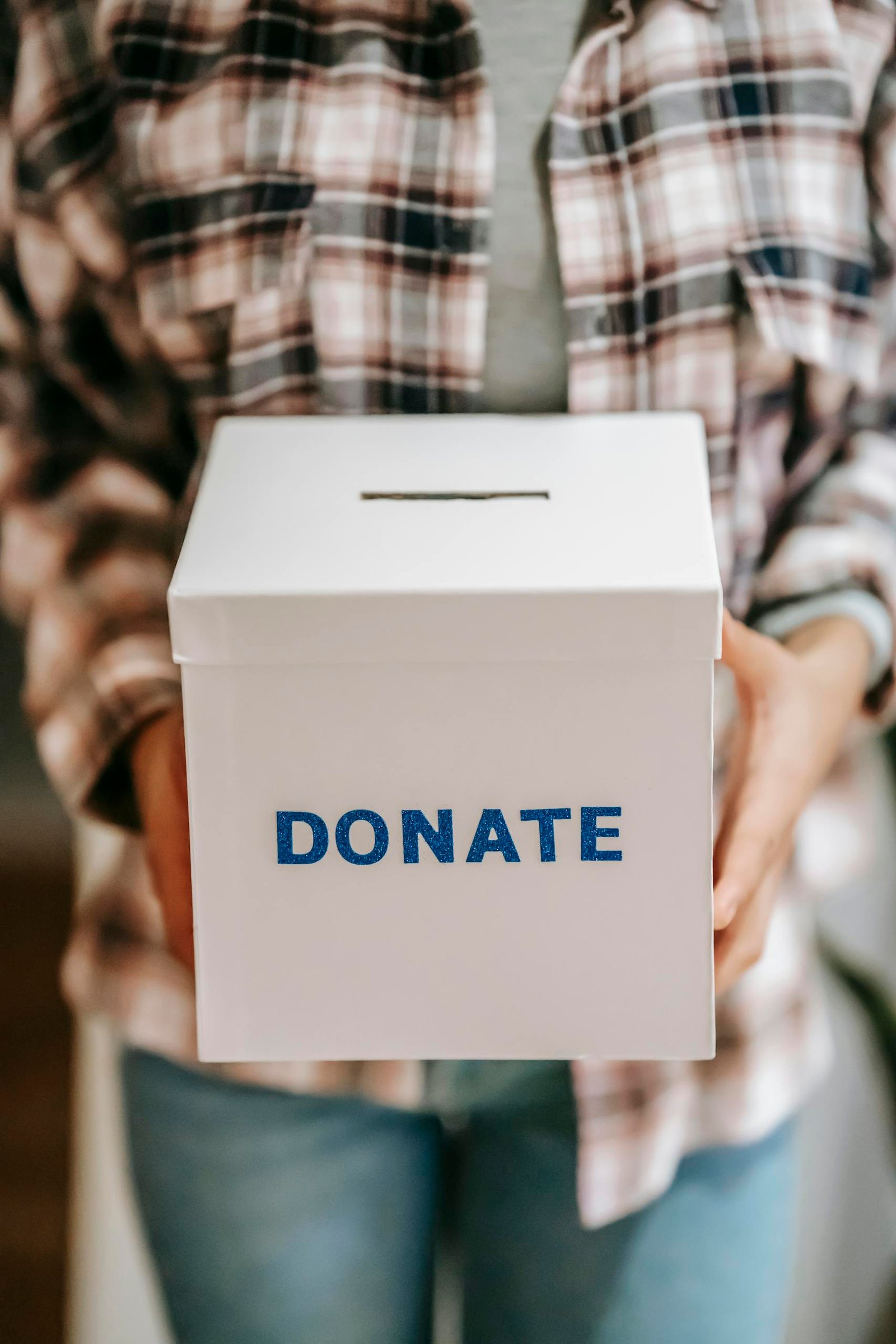 Close-up of a person holding a 'donate' box, encouraging charity and support.